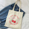 A beige canvas shopping bag with pink cherry embroidery on top, resting on a blue denim shirt.