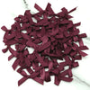 A pile of small, deep burgundy satin ribbon bows for crafts and decor.