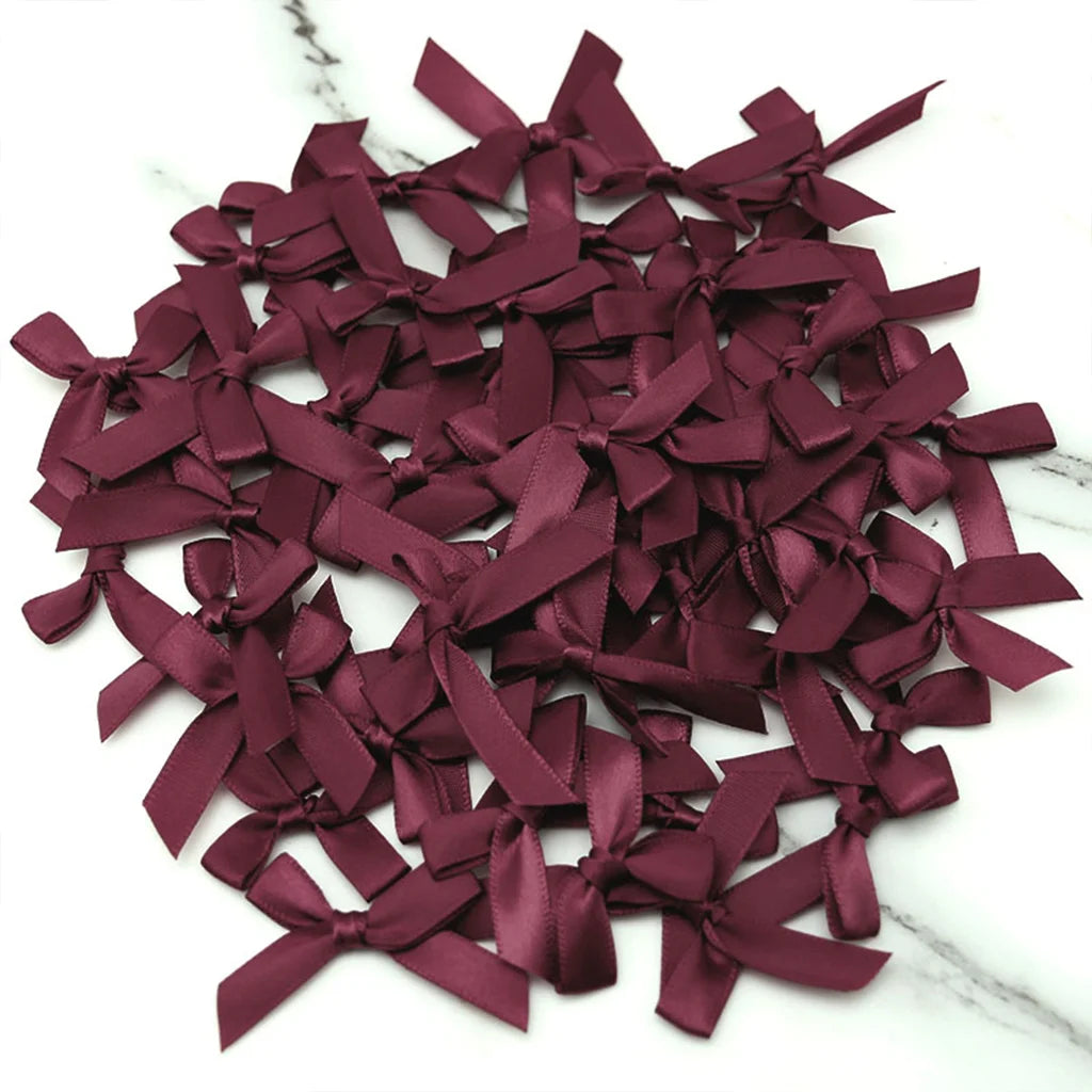 A pile of small, deep burgundy satin ribbon bows for crafts and decor.