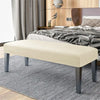 A beige velvet bench slipcover with dark gray legs placed on a striped rug in a bedroom setting.