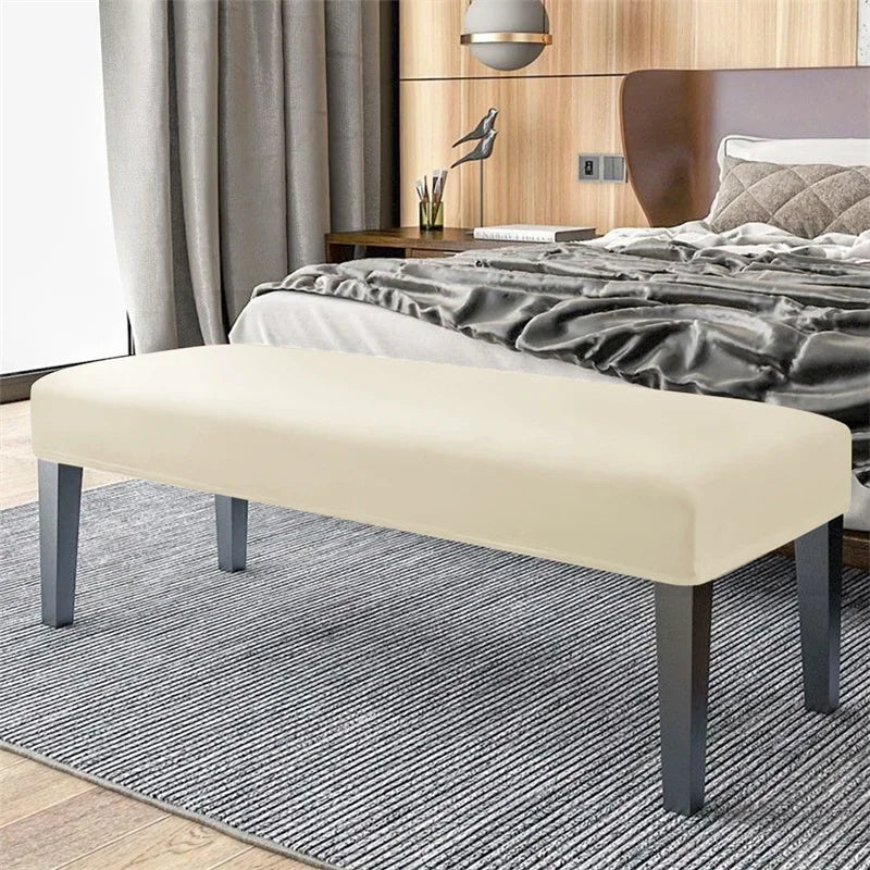 A beige velvet bench slipcover with dark gray legs placed on a striped rug in a bedroom setting.
