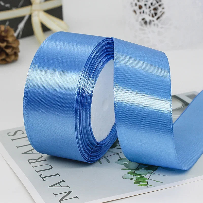 A roll of light blue satin ribbon is shown unwound, lying on a piece of paper.