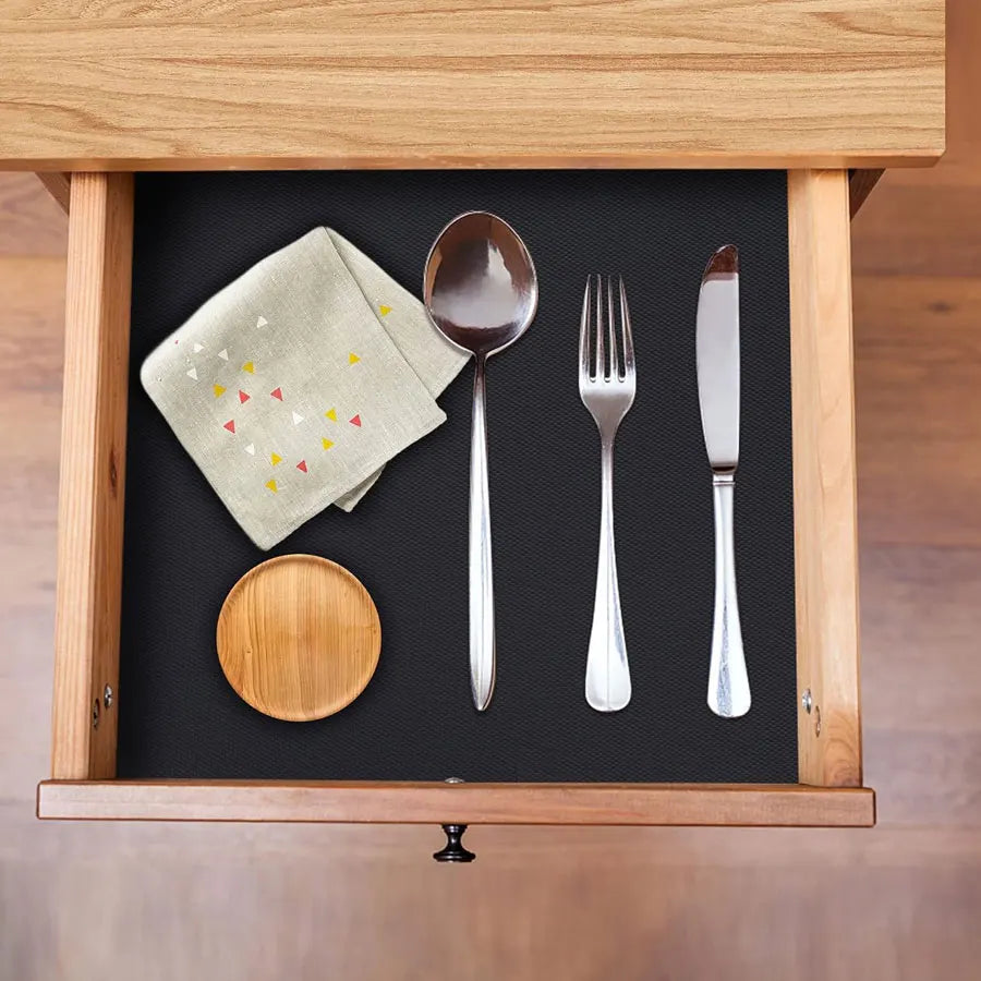 A wooden drawer organizer holds silverware, a spoon, and a small wooden plate on a black lining.