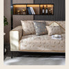 A luxury chenille sofa cover in beige and gold tones displayed on a modern sofa with dark wood shelving.