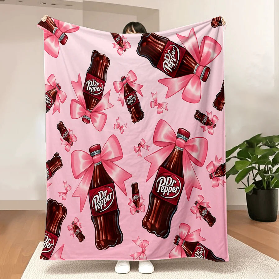 A pink cozy blanket featuring a repeating pattern of Dr. Pepper bottles with pink ribbons.