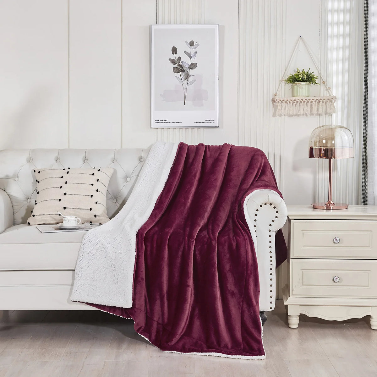 A deep burgundy sherpa fleece blanket draped over a white sofa in a bright, modern living room.