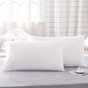 White microfiber pillow covers displayed on a bed with sheer curtains in the background.