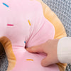 A hand is touching the pink fabric of a Kawaii Fried Doughnut plush pillow cushion.
