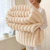 A woman holds a thick, fluffy, cream-colored blanket with horizontal stripes.