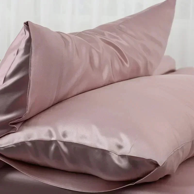 A set of smooth, rosy pink satin silk pillows resting on a surface.