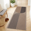 A long runner rug with geometric stripes in beige and black tones placed on a light wood floor.
