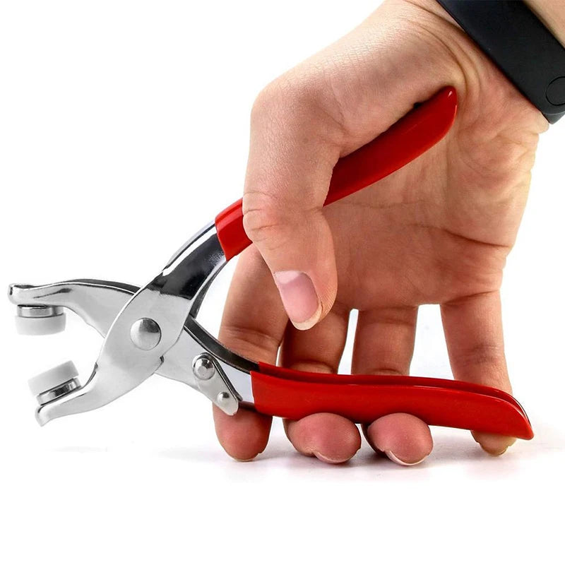 A hand is holding a red and silver precision snap button kit pliers for DIY sewing and crafts.