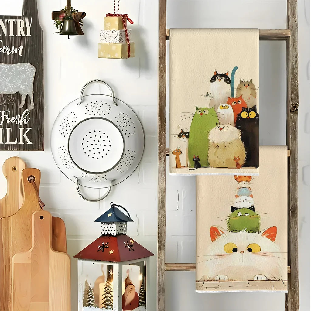 A set of two cat-themed kitchen towels featuring various cats in watercolor style hanging on a wooden rack.