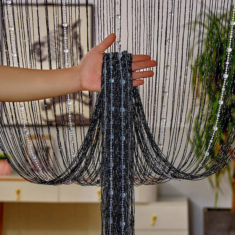 A hand is holding a black beaded string curtain, showing the delicate crystal strands and draping fabric.