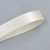 A roll of cream-colored satin ribbon shown diagonally against a light gray patterned background.