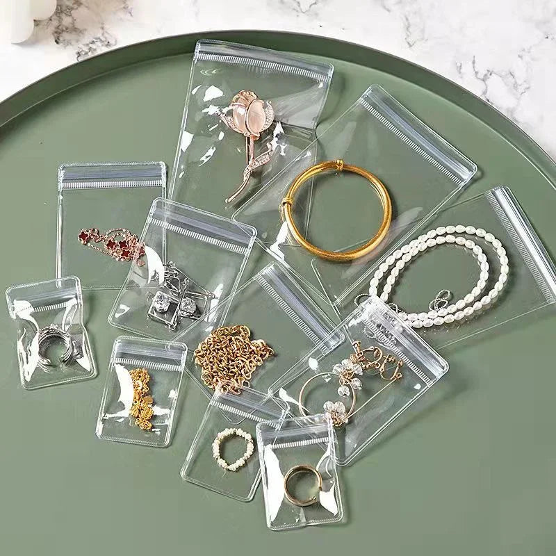 Clear plastic self-sealing jewelry storage bags filled with various gold and silver rings, necklaces, and earrings arranged o