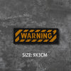 A black embroidered warning badge with yellow text on a dark gray textured background, size 9x3cm.