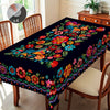 A dark floral tablecloth with colorful embroidery and embossed edges displayed on a wooden dining table.