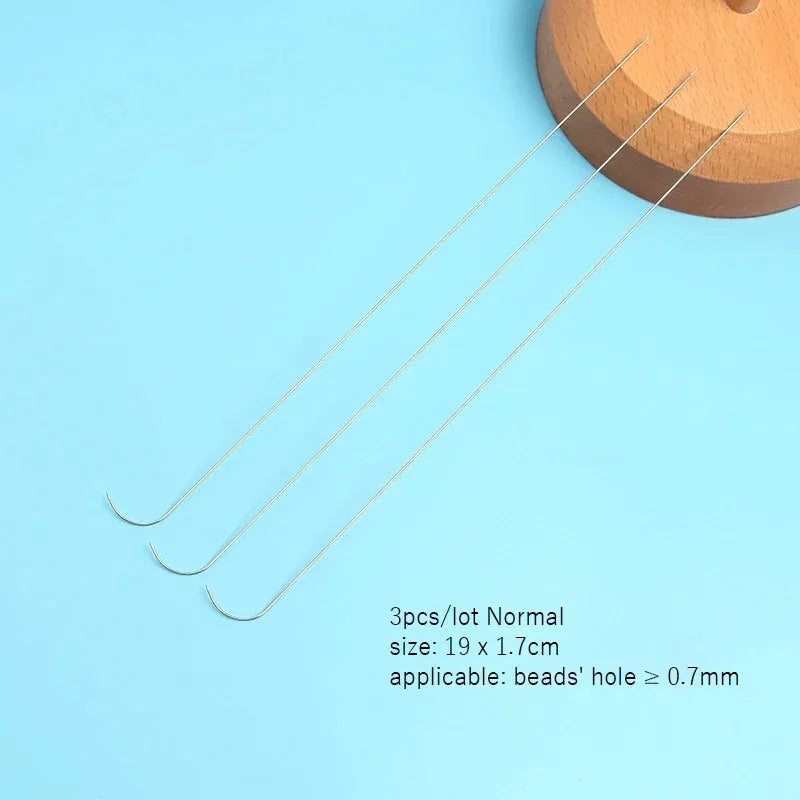 A set of three stainless steel beading needles laid diagonally on a light blue surface.