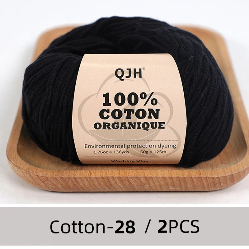 A ball of black 100% organic cotton yarn labeled QJH for knitting and crochet on a wooden tray.