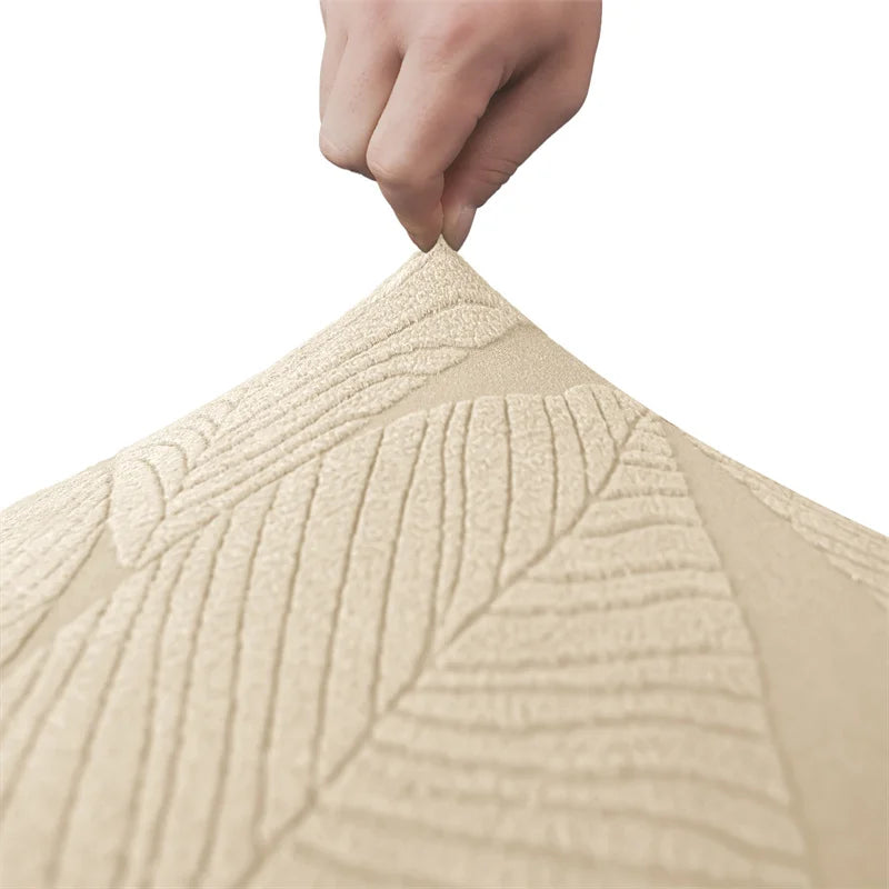 A hand is touching the textured fabric of a beige jacquard ottoman footrest slipcover.