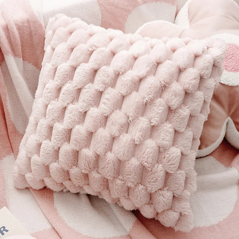 A fluffy pink quilted decorative plush pillow cover resting on a light pink fabric background.