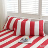 A set of three red and white striped pillows resting on a red and white striped bed, near a window.