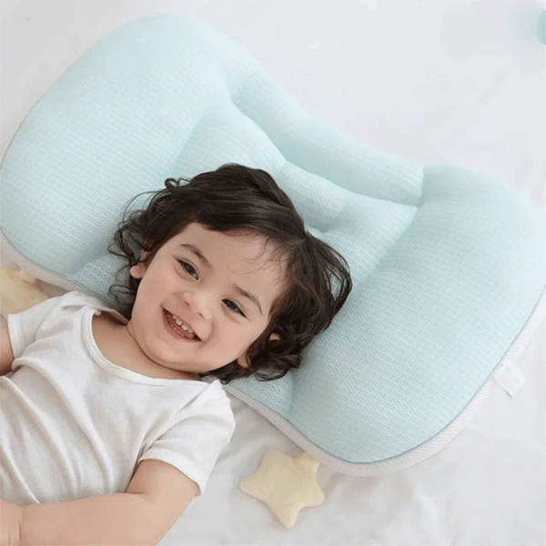 A smiling baby is lying on a light blue breathable sleep pillow with a yellow star accessory.