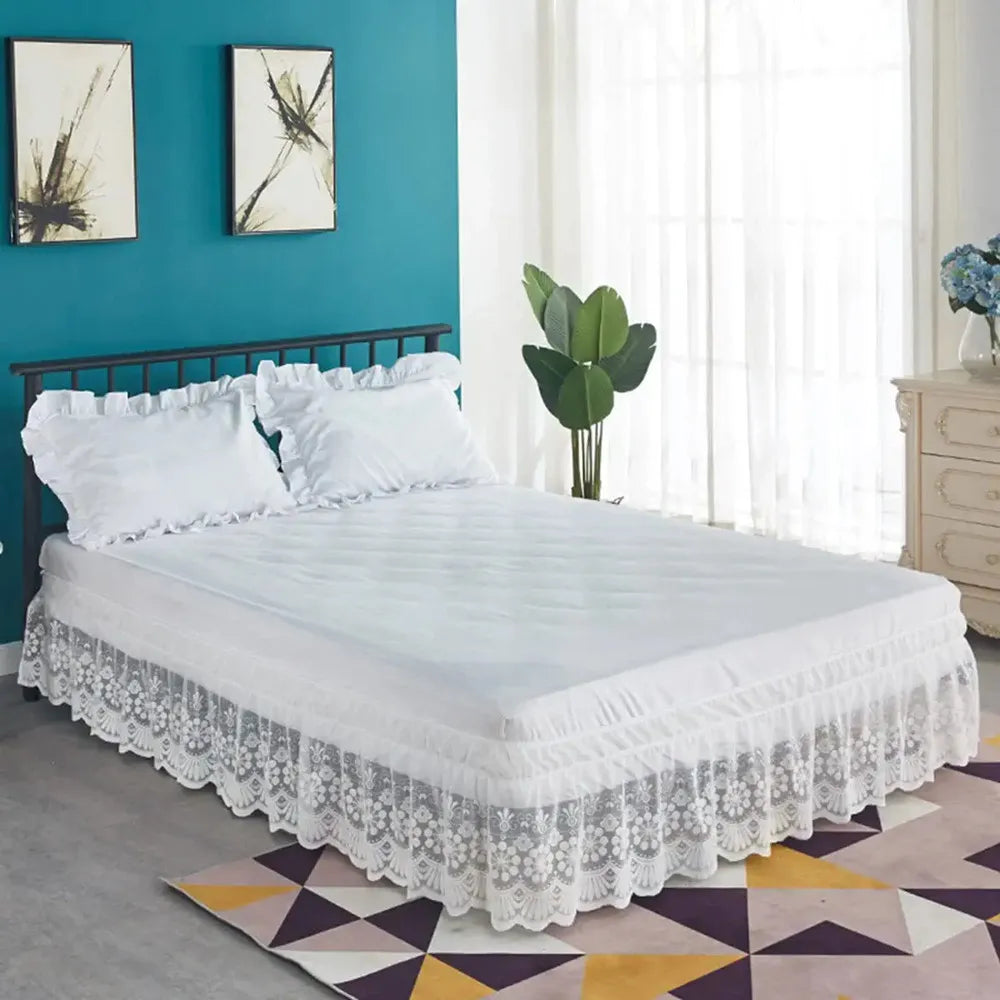 A white bed with a lace ruffle skirt and elastic trim set against a teal wall.