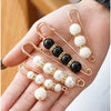 A hand holds an adjustable pearl brooch featuring black and white beads on gold-toned wire.
