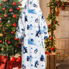 A white sherpa fleece blanket hoodie with a blue and black penguin pattern displayed next to Christmas decorations.