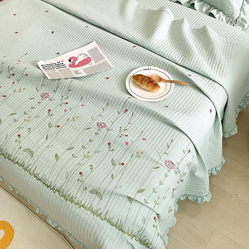 A light mint green floral embroidery quilt bedspread set with a rolled croissant on top.
