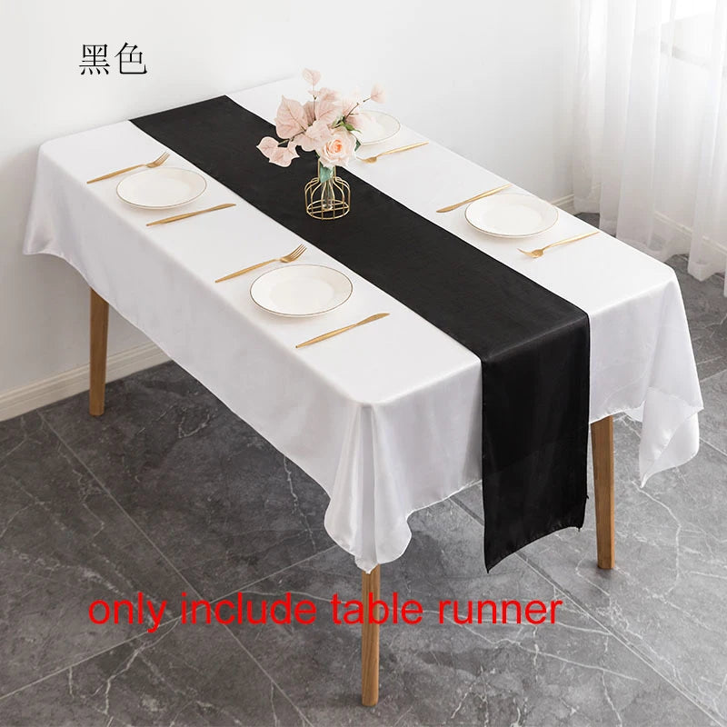 Black satin table runner on a white tablecloth set for dining with pink floral centerpiece