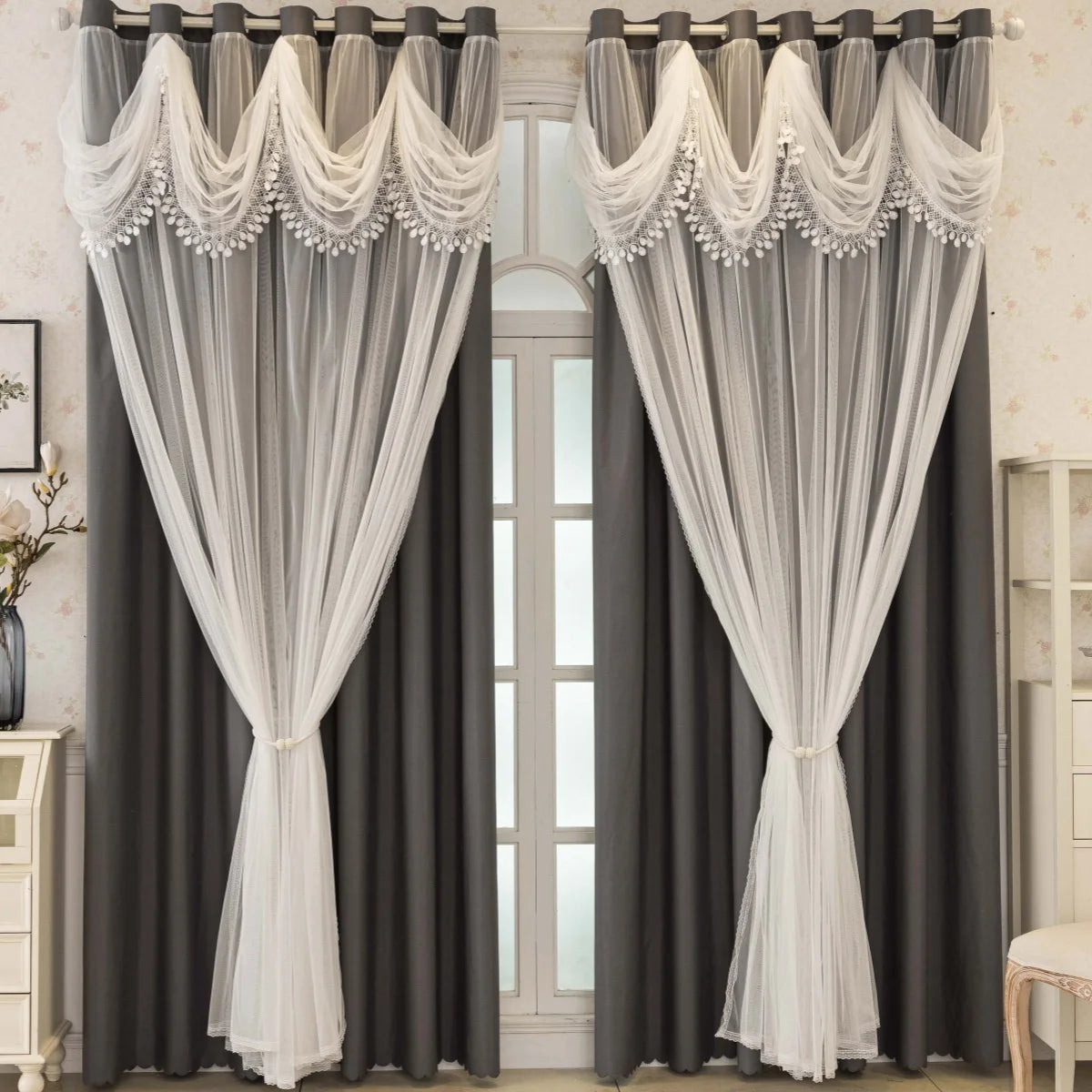Pair of gray blackout curtains with white wave pattern trim and sheer fabric hanging in a doorway.