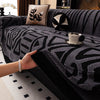 A hand is placing a cup on a dark gray knitted sofa protector with black geometric patterns.