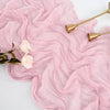 Pink sheer gauze fabric draped elegantly with gold-toned decorative spoons on a white surface.