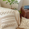 A close-up of a cream knit pillow cover with textured trim resting on a light colored sofa or bed.