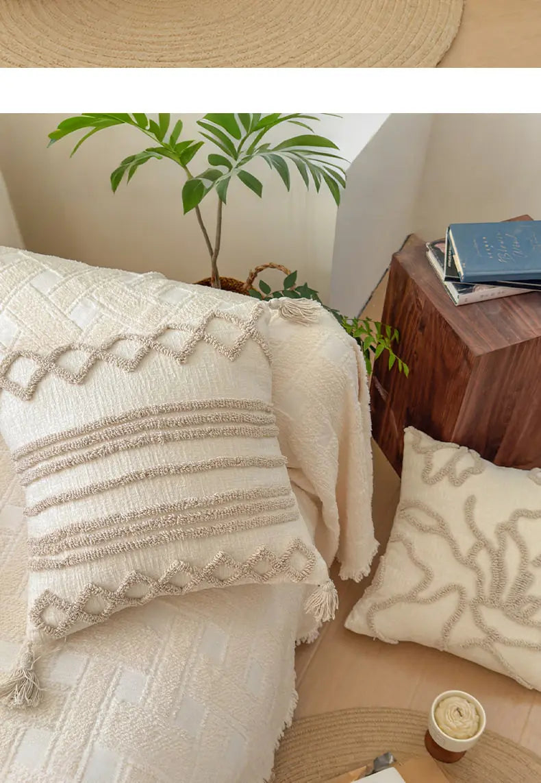 A close-up of a cream knit pillow cover with textured trim resting on a light colored sofa or bed.