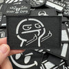 A close-up view of black tactical patches with white graphic designs and text on a hand.