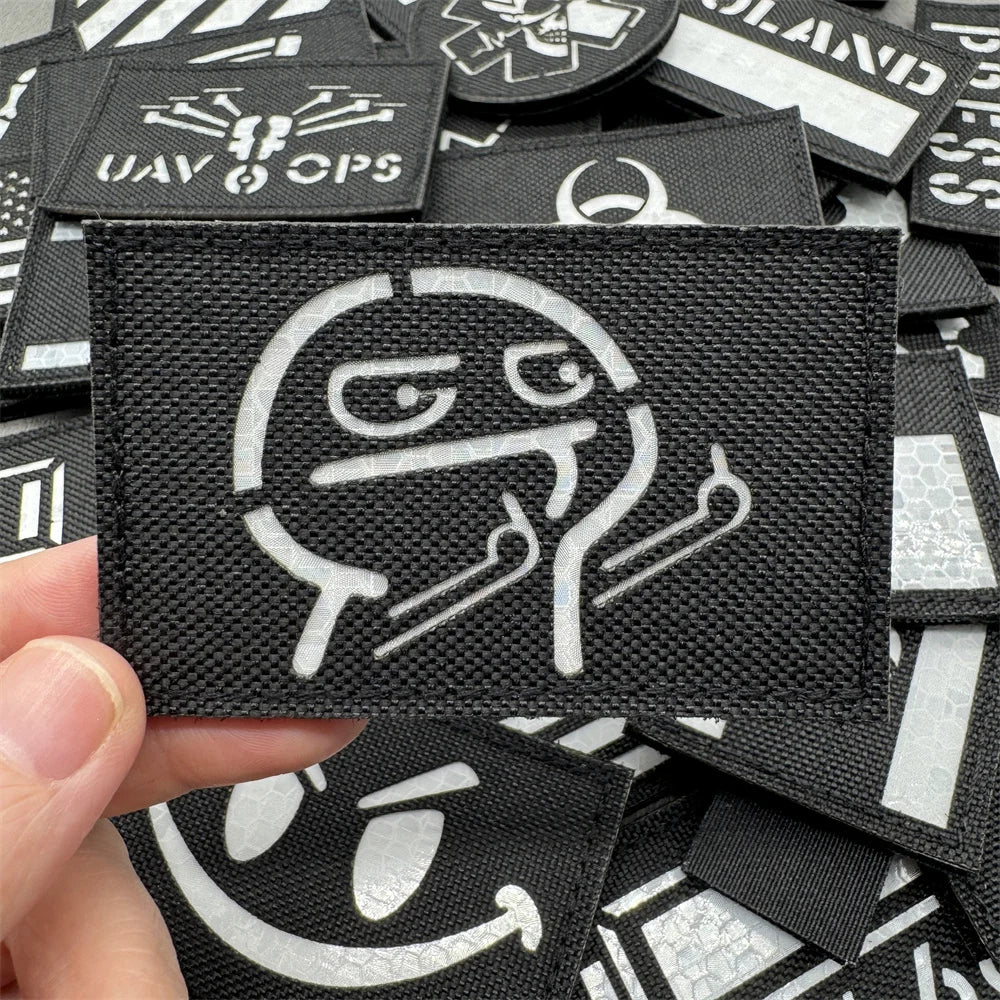 A close-up view of black tactical patches with white graphic designs and text on a hand.
