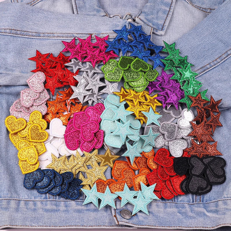 A collection of colorful glitter iron-on embroidered love heart and star patches arranged in a radial pattern on denim fabric