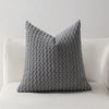A gray knitted decorative pillow cover with a textured, dimpled pattern sits on a white sofa.