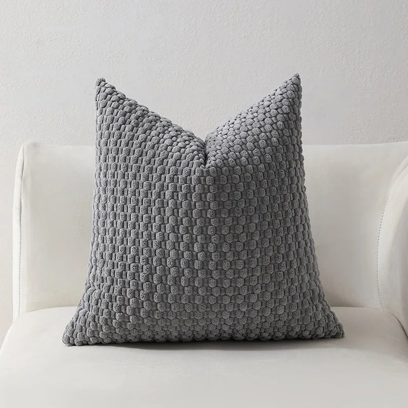 A gray knitted decorative pillow cover with a textured, dimpled pattern sits on a white sofa.