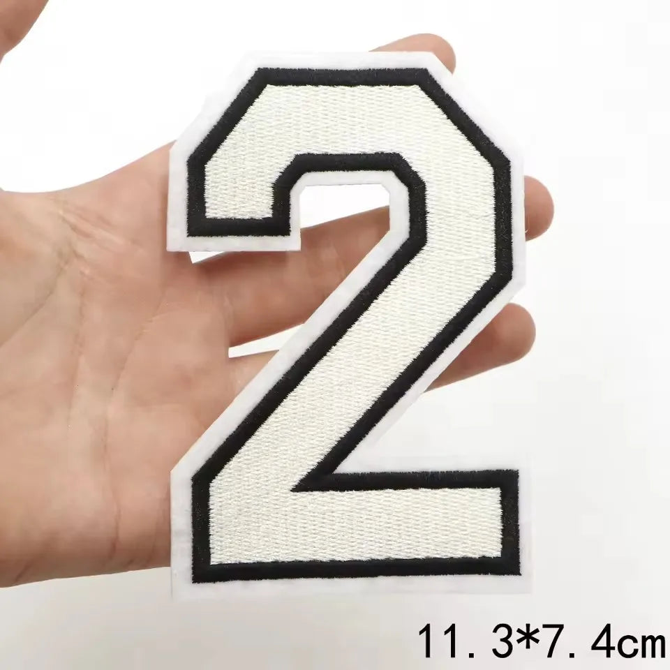 A white felt letter patch shaped like the number 2 is held in a hand.