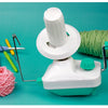 A white hand-operated wool yarn winder device with a green knob and a ball of pink yarn.