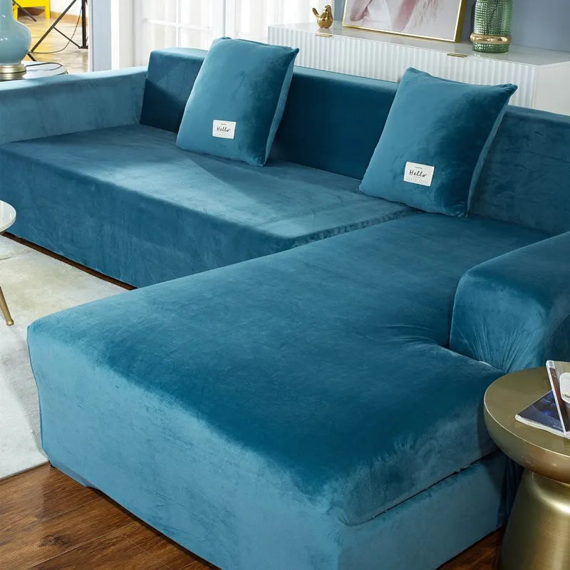 A deep teal velvet sofa cover featuring light blue accent pillows on an L-shaped sectional sofa.