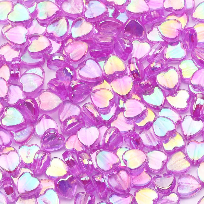 A close-up of small, iridescent pink and purple acrylic heart beads for jewelry making.