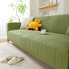 A lime green stretchable sofa cover with a vertical line pattern featuring a yellow stuffed animal and white pillows.