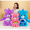 Three Care Bears plush toys in purple, pink, and blue sitting on a white surface.