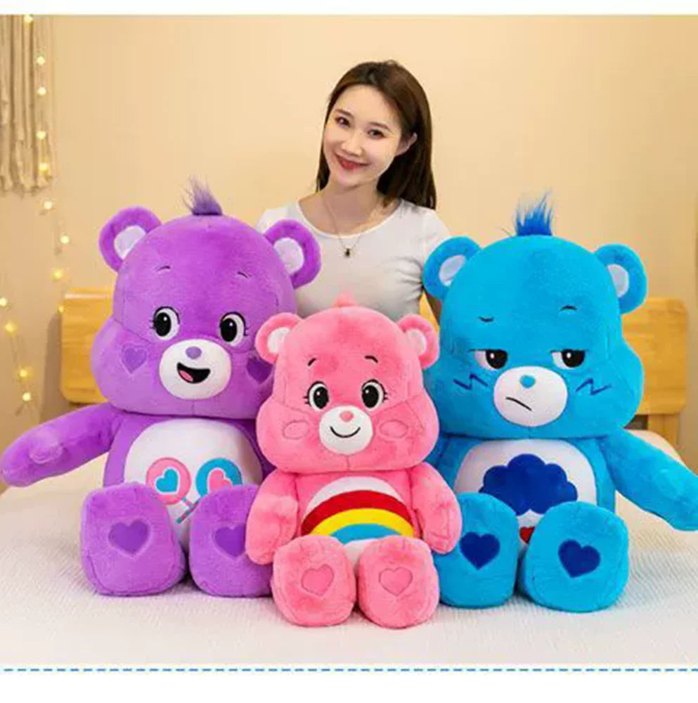 Three Care Bears plush toys in purple, pink, and blue sitting on a white surface.